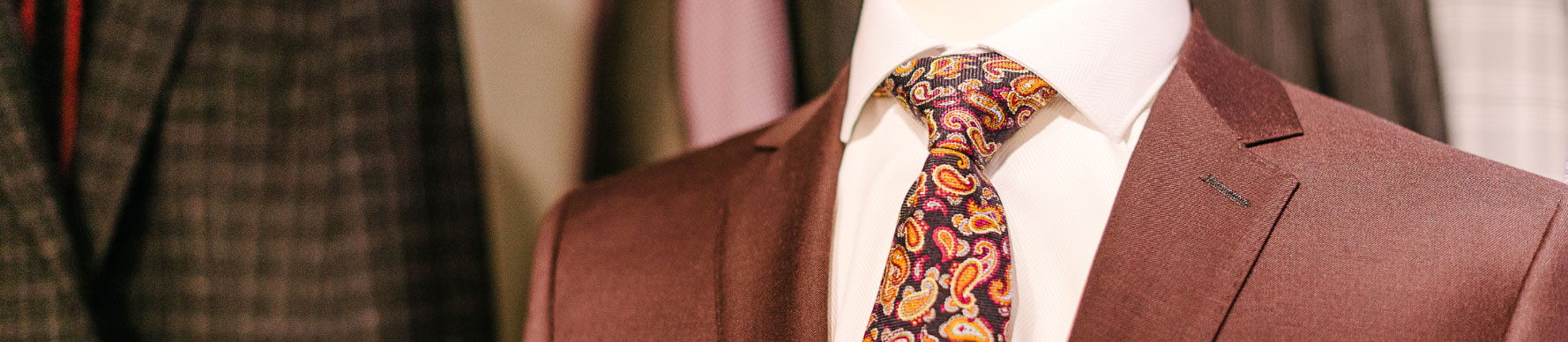 SUITS-LeadImage A display of a burgundy jacket over a white dress shirt. There is a colorful tie and white pocket square